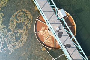 Aerial view of a wastewater treatment plant with a teal walkway crossing a circular tank. 