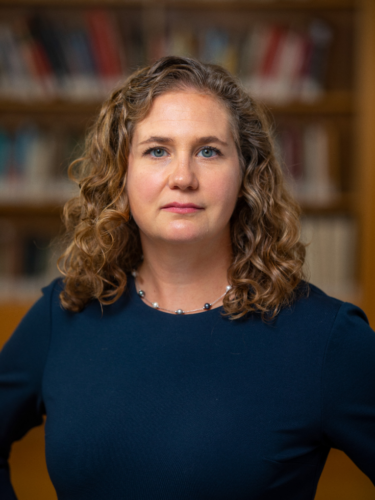 Jennifer Nuzzo smiles at the camera while standing in front of a book case.