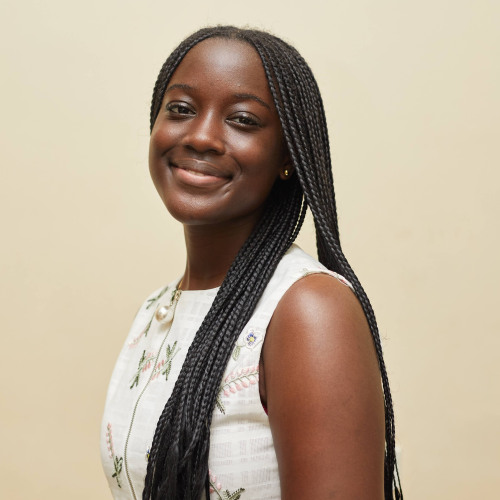 Danica Damoah stands 3/4 turn smiling at camera while standing in front of a white wall.