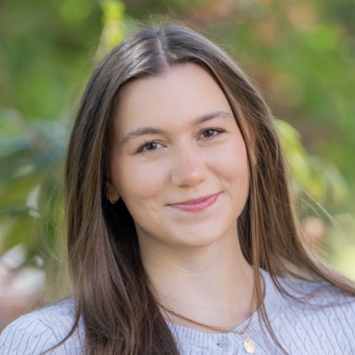 Yuliya Velhan smiles at camera while standing outdoors in front of a tree. 